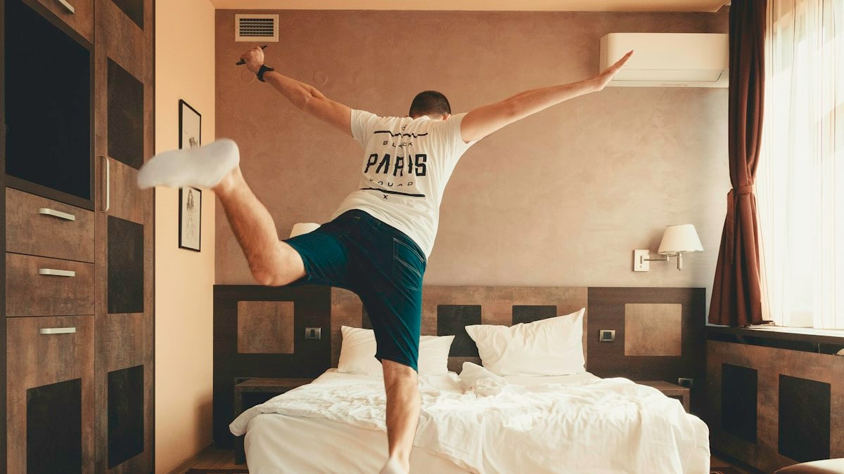 man wearing white shirt about to jump on bed